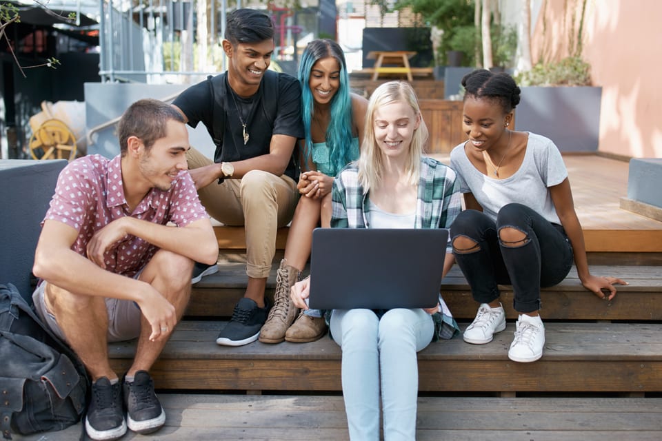 Cheerful friends looking at a laptop together on campus