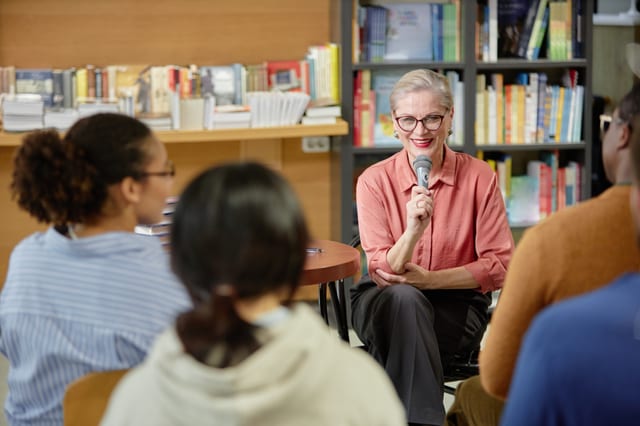 A woman with a microphone presenting to a small audience
